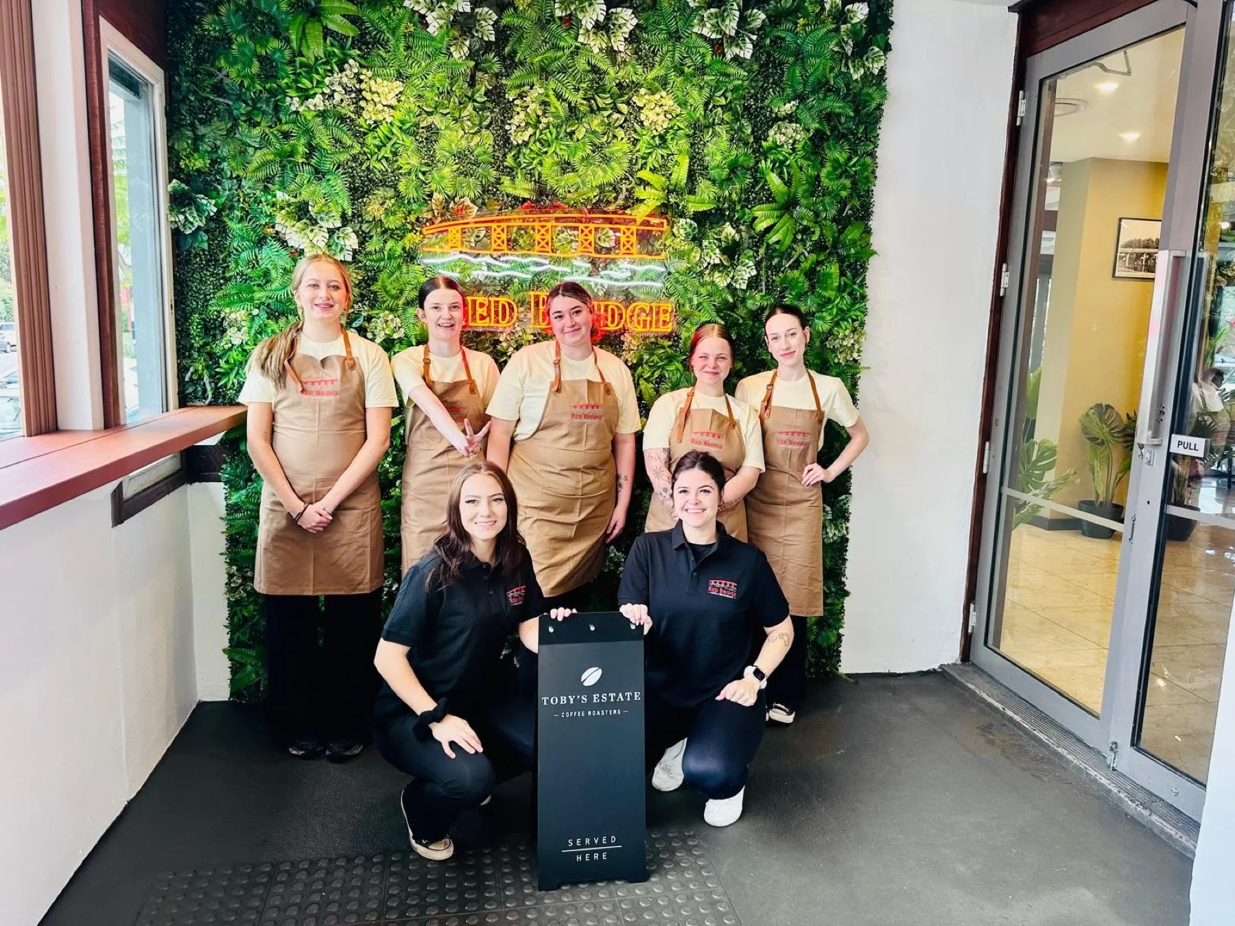 The Red Bridge cafe team together at the green wall